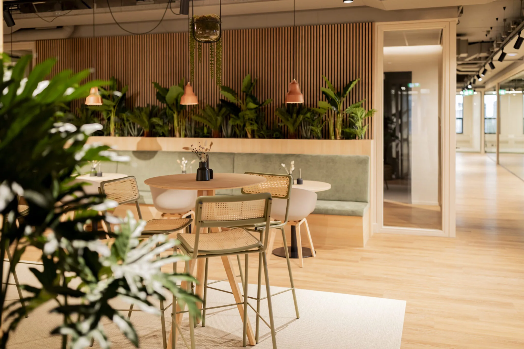 Modern ingerichte lounge- en werkruimte in EO Diemen met houten meubels, groen zitbankje en veel planten.