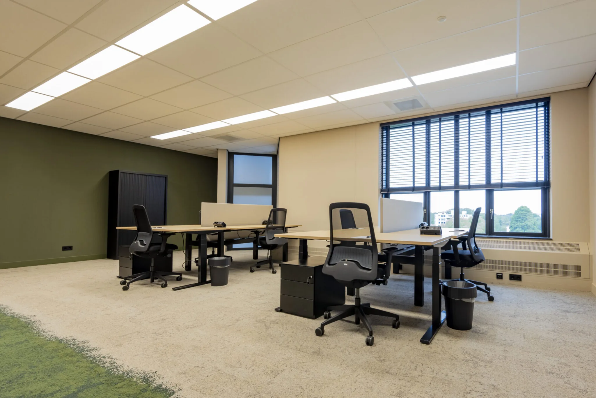 Modern ingericht kantoor in EO Diemen met bureaus, bureaustoelen en grote ramen met lamellen.