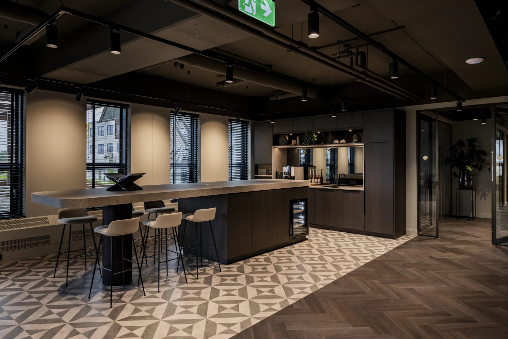 Moderne kantoorkeuken in EO Diemen met een centraal eiland, barkrukken en geometrisch tegelpatroon op de vloer.