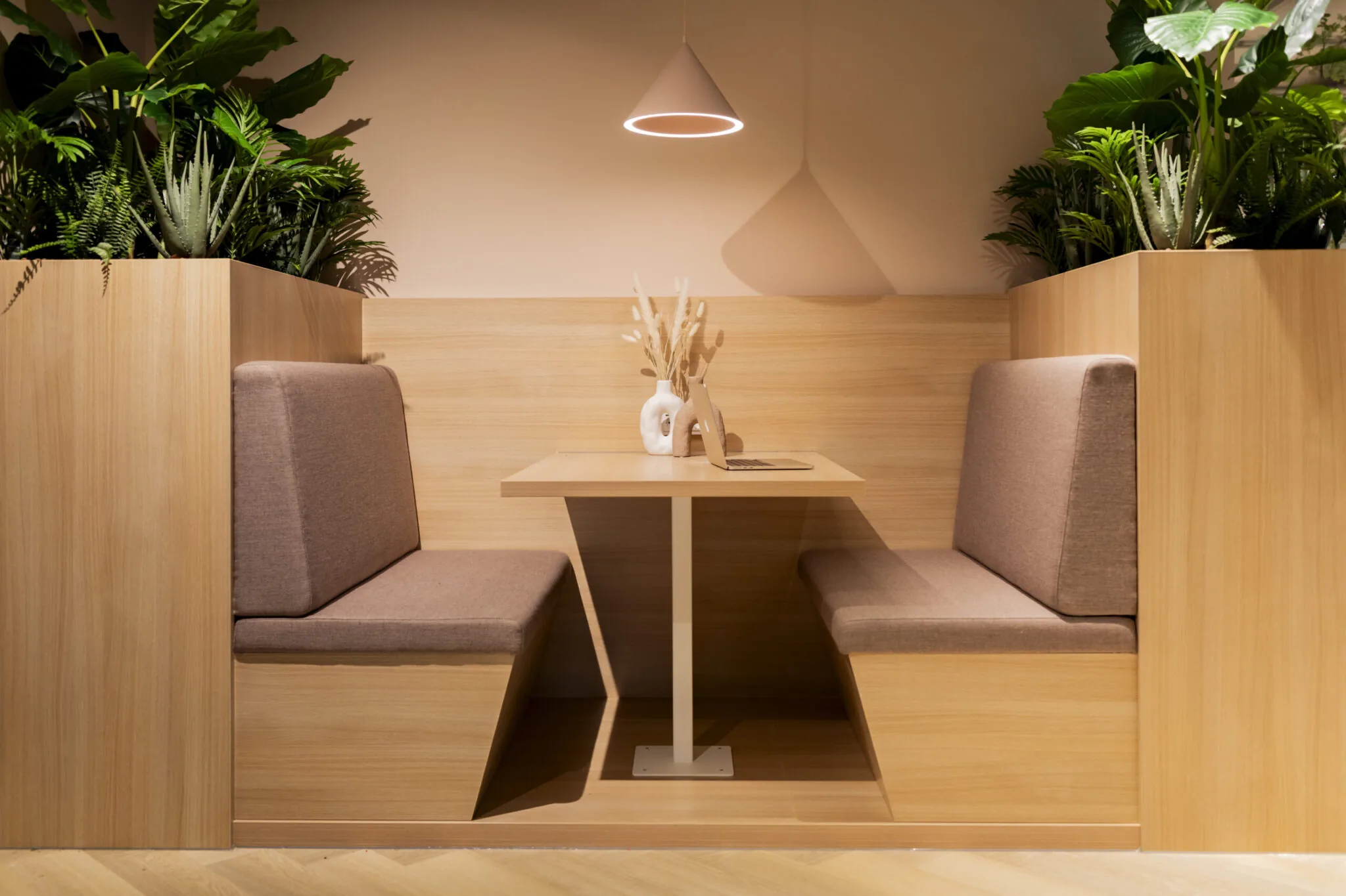 Moderne houten werk- of zithoek EO_Diemen_233 met tegenover elkaar geplaatste zitbanken, een tafel, laptop en groene planten.