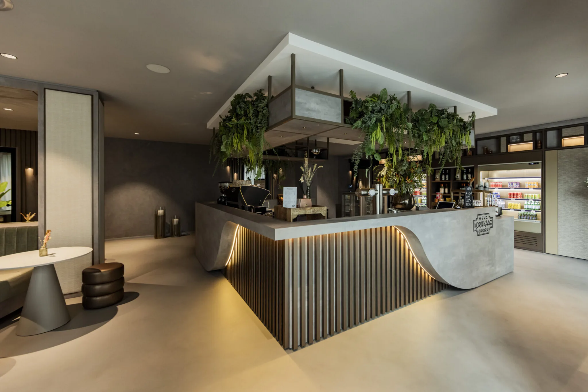 Modern ingerichte ontvangst- en horecaruimte in EO Diemen met een strak betonnen counter, sfeerverlichting en hangende groene planten.