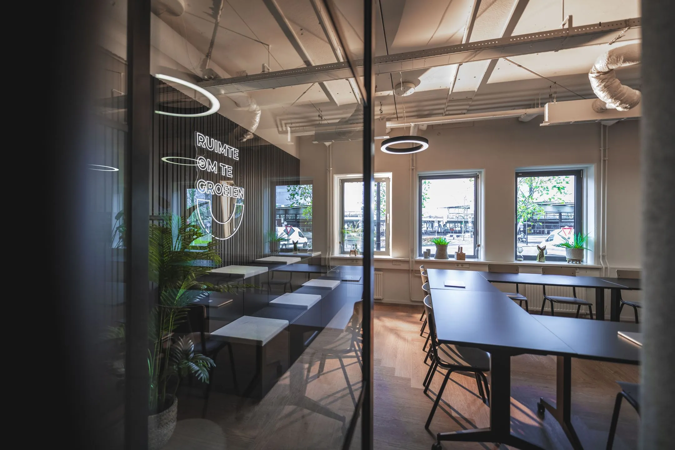 Moderne kantoorruimte aan de Egbert Gorterstraat met werkplekken, grote ramen en een neonbord met de tekst "Ruimte om te groeien".