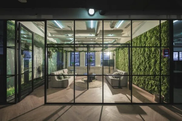 Moderne vergaderruimte aan de Egbert Gorterstraat 2-14 met groene moswanden, glazen wanden en comfortabele zitbanken.
