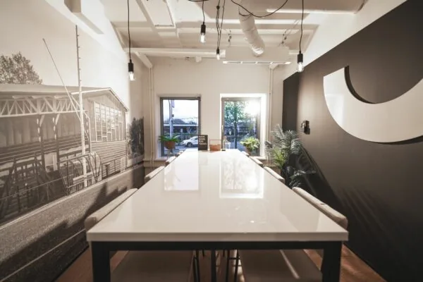 Vergaderruimte aan de Egbert Gorterstraat met een lange witte tafel, industriële verlichting en muurdecoratie met een zwart-wit foto van een tribune.