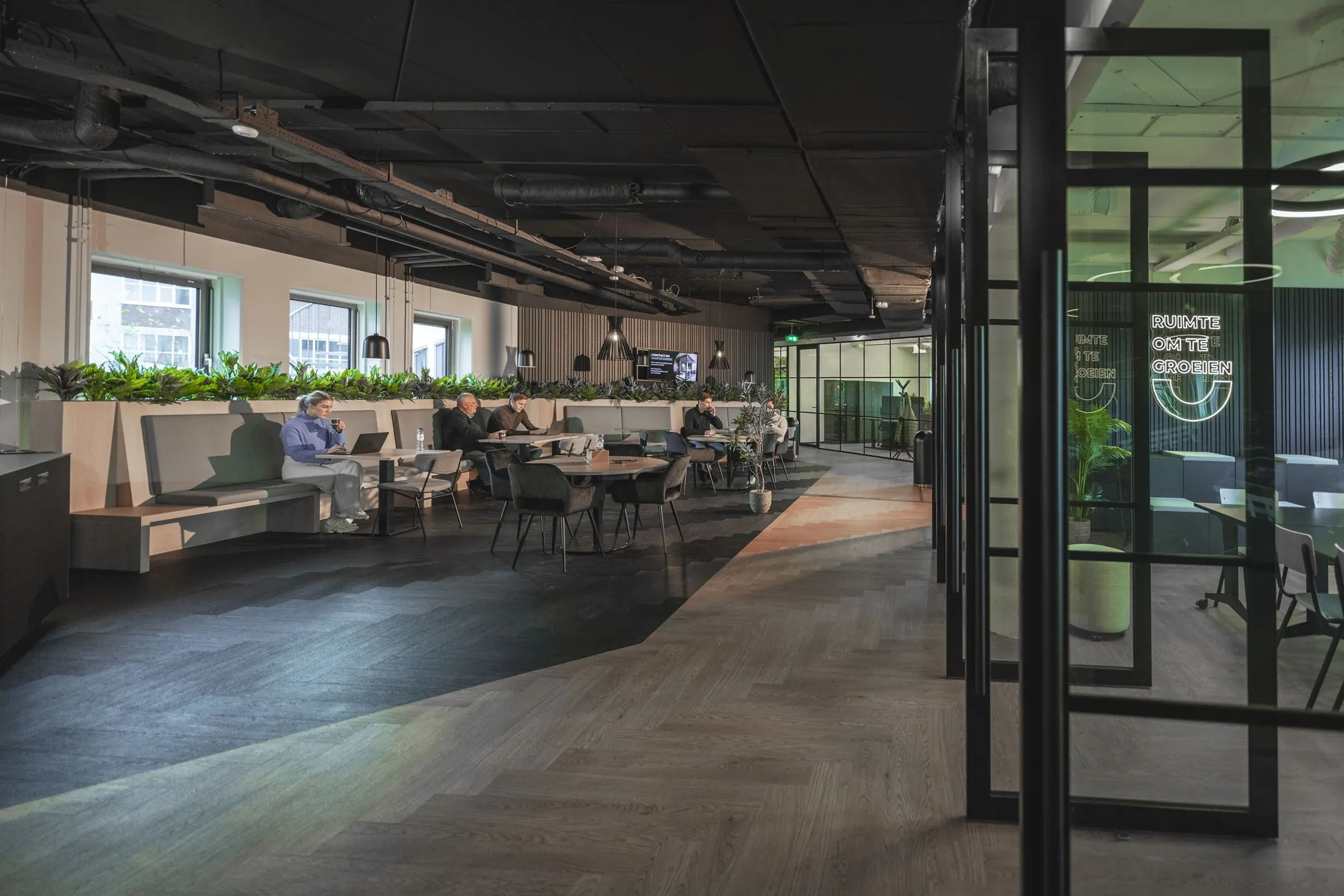 Moderne werkruimte aan de Egbert Gorterstraat 2-14 met zitgedeelte, planten en glazen vergaderruimtes.