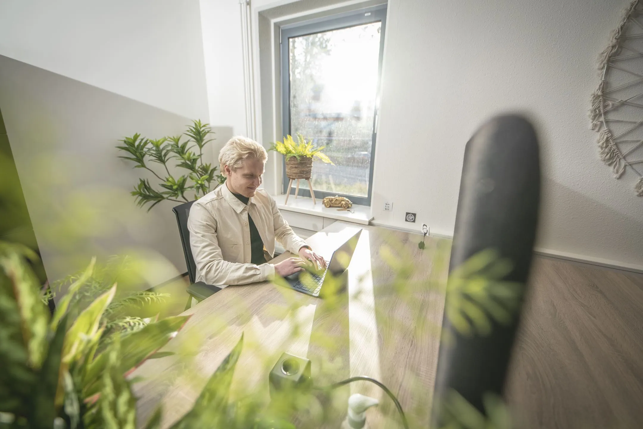 Man werkt op een laptop aan een bureau in een licht en modern kantoor aan de Egbert Gorterstraat, omringd door planten.