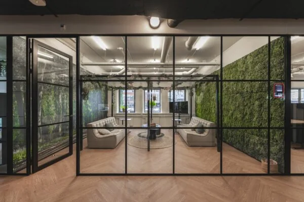 Moderne vergaderruimte aan de Egbert Gorterstraat 2-14 met glazen wanden, groene moswanden en comfortabele zitbanken.