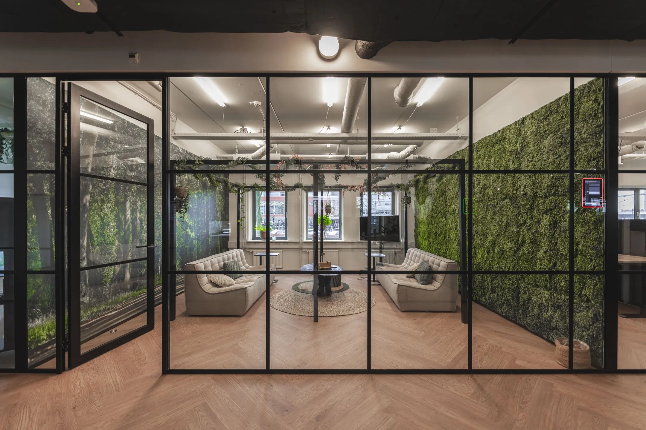 Moderne vergaderruimte aan de Egbert Gorterstraat 2-14 met glazen wanden, groene moswanden en comfortabele zitbanken.