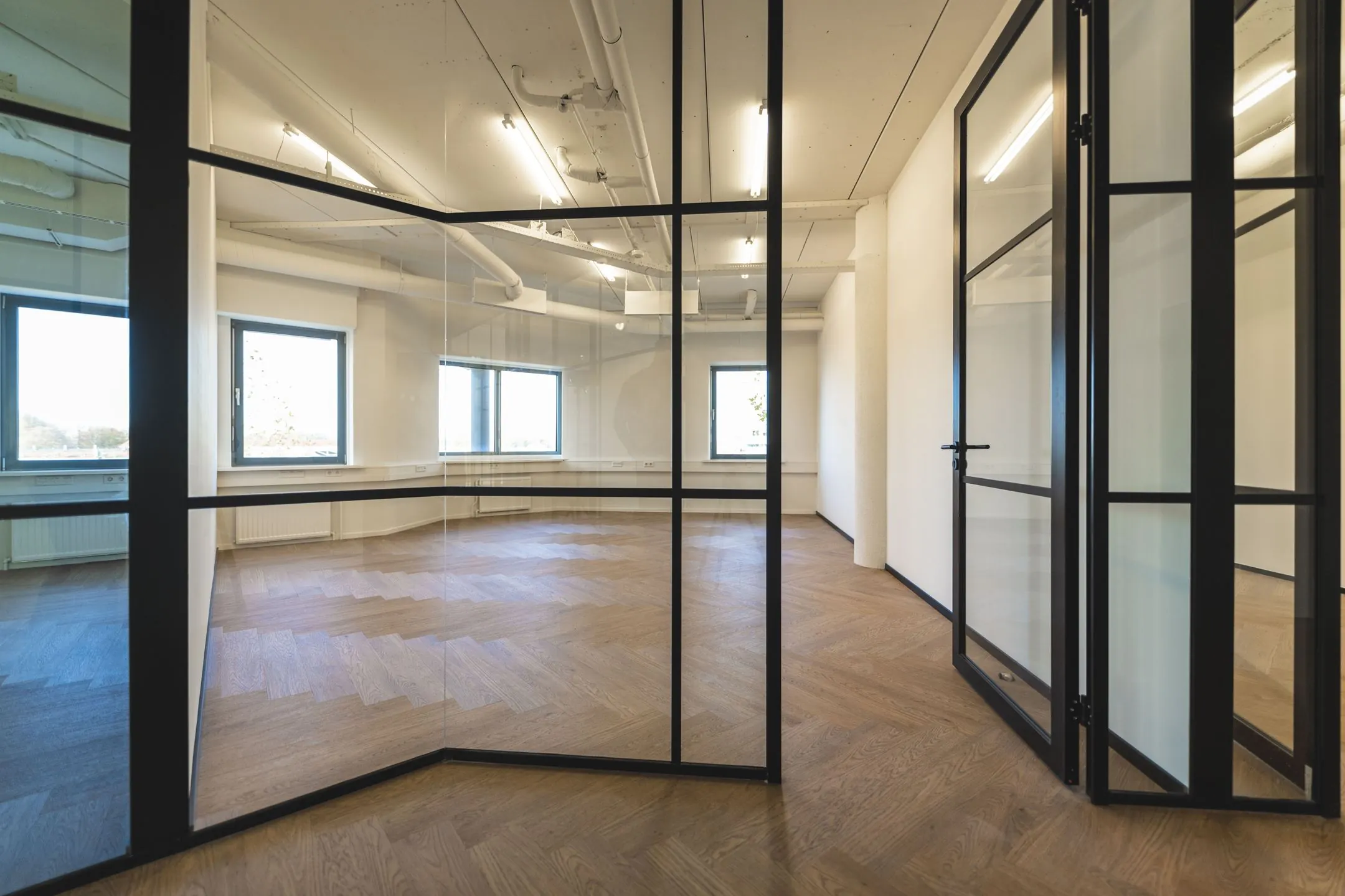 Moderne kantoorruimte aan de Egbert Gorterstraat 2-14 met glazen wanden, visgraat houten vloer en grote ramen.