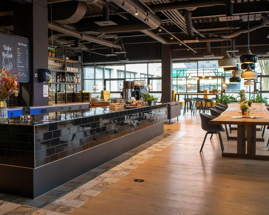 Moderne en sfeervolle horecagelegenheid in Enschede met een zwarte tegelbar, houten tafels en veel natuurlijk licht.