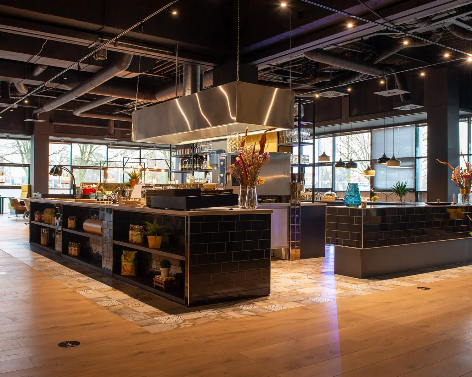 Moderne open keuken met zwarte tegels, houten vloer en sfeervolle verlichting in een restaurant in Enschede.