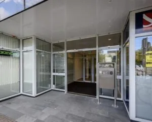 Glazen entree van een kantoorgebouw met schuifdeuren en intercomsysteem.