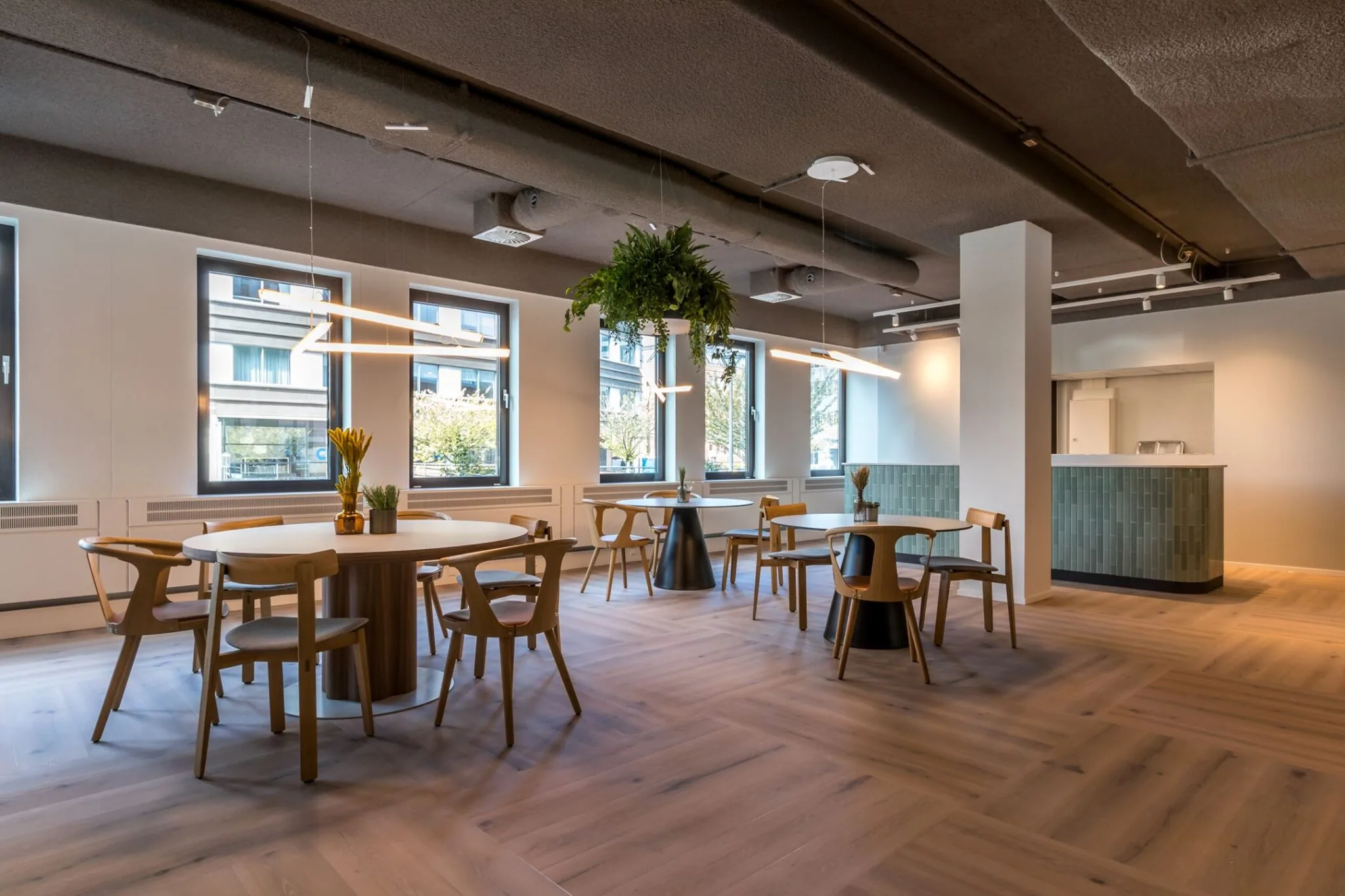 Moderne, lichte kantine met ronde tafels, houten stoelen, hangplanten en een betegelde bar bij Euclideslaan 265.