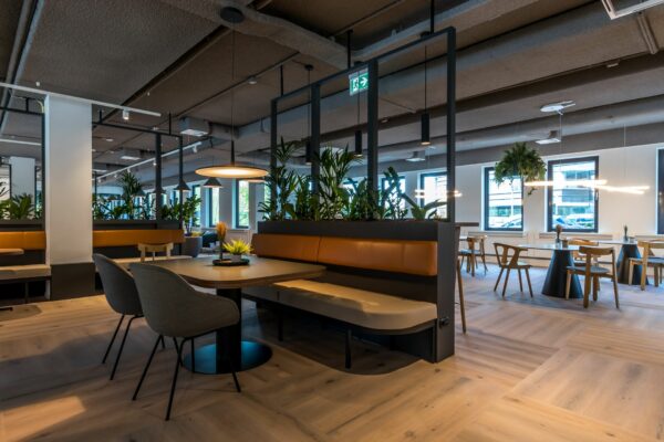 Moderne en sfeervolle kantoorcafetaria in Euclideslaan 265 met houten vloer, designmeubilair en groene planten.