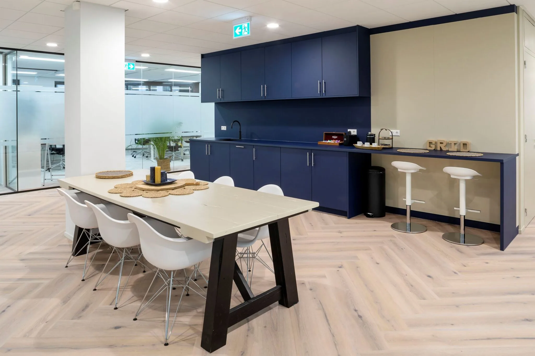 Moderne kantoorkeuken met blauwe kasten, een lange eettafel en barkrukken bij Euclideslaan 265.