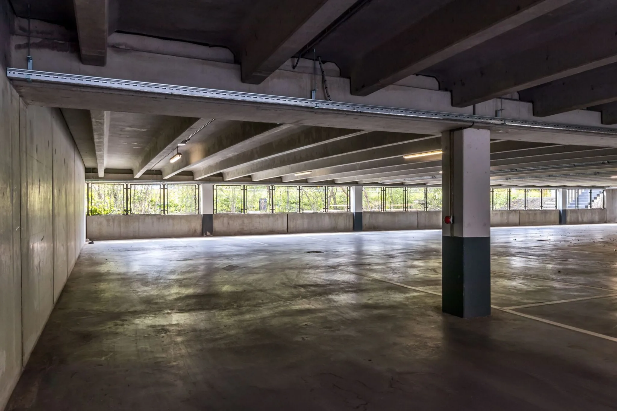 Leeg parkeerdek in een betonnen parkeergarage aan de Euclideslaan 265 met grote ramen en zicht op groen.