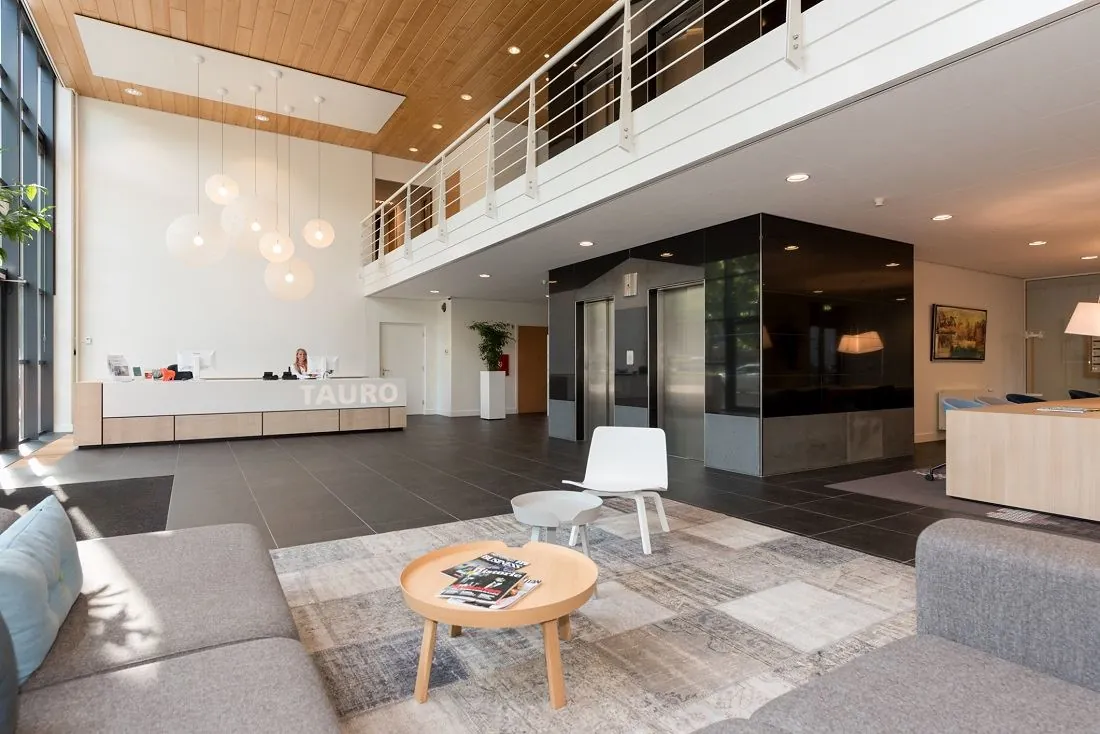 Moderne ontvangsthal van het kantoorpand aan de Europalaan 16 met receptiebalie, zithoek en liften.
