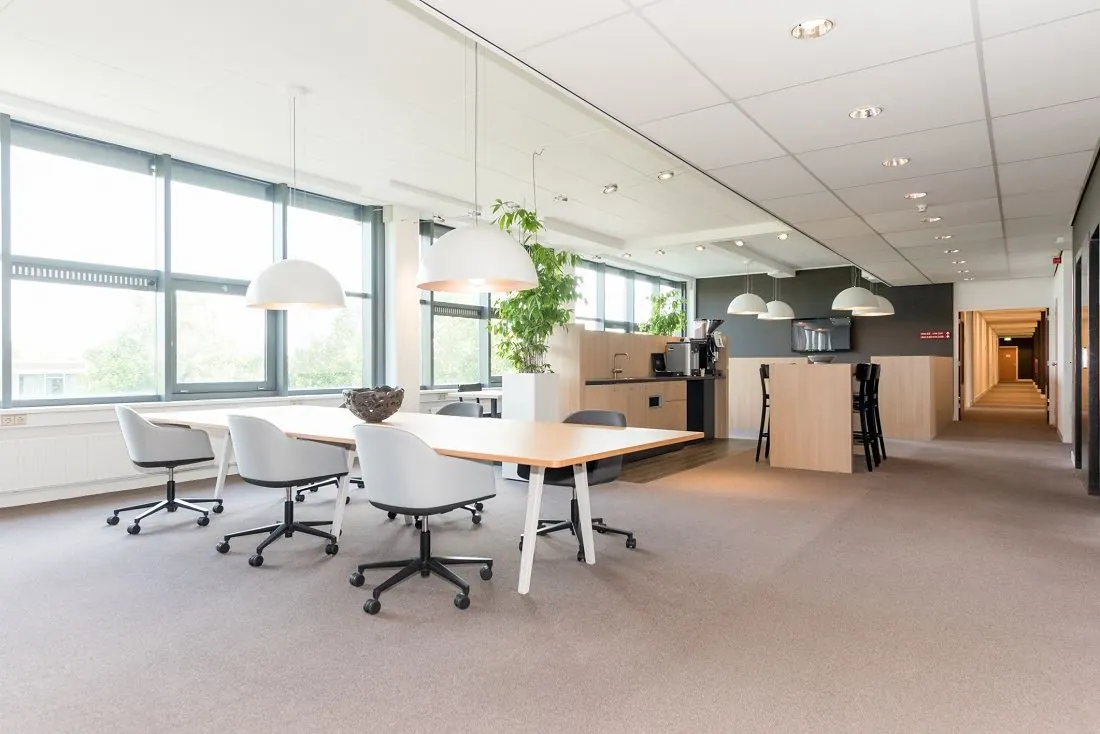 Moderne kantoorruimte aan de Europalaan 16 met vergadertafel, zitstoelen en een kitchenette met koffiehoek.