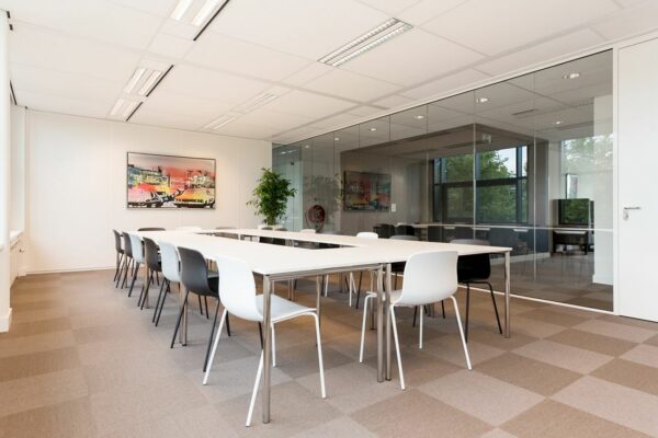 Moderne vergaderruimte aan de Europalaan 16 met strakke witte tafels, zwart-witte stoelen en een glazen wand.