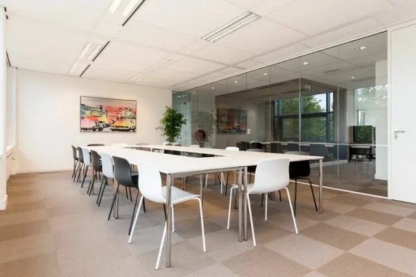 Moderne vergaderruimte aan de Europalaan 16 met strakke witte tafels, zwart-witte stoelen en een glazen wand.