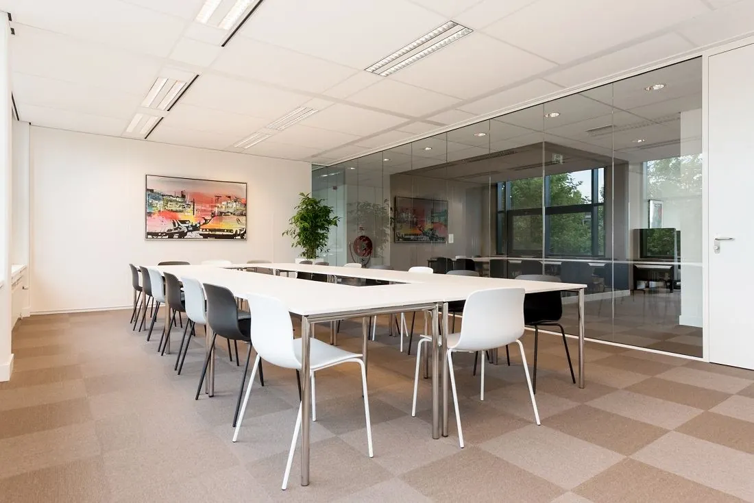 Moderne vergaderruimte aan de Europalaan 16 met strakke witte tafels, zwart-witte stoelen en een glazen wand.