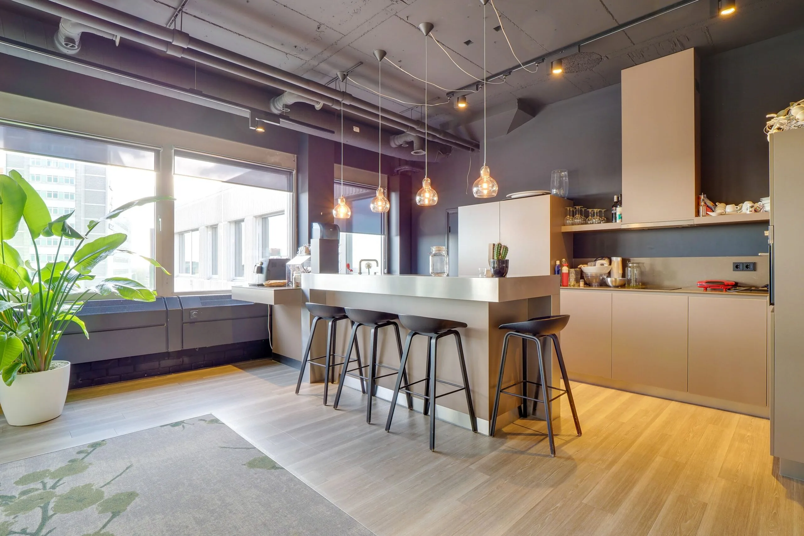 Moderne kitchenette met kookeiland, barkrukken en hanglampen in een kantoorruimte aan de Europalaan 400.
