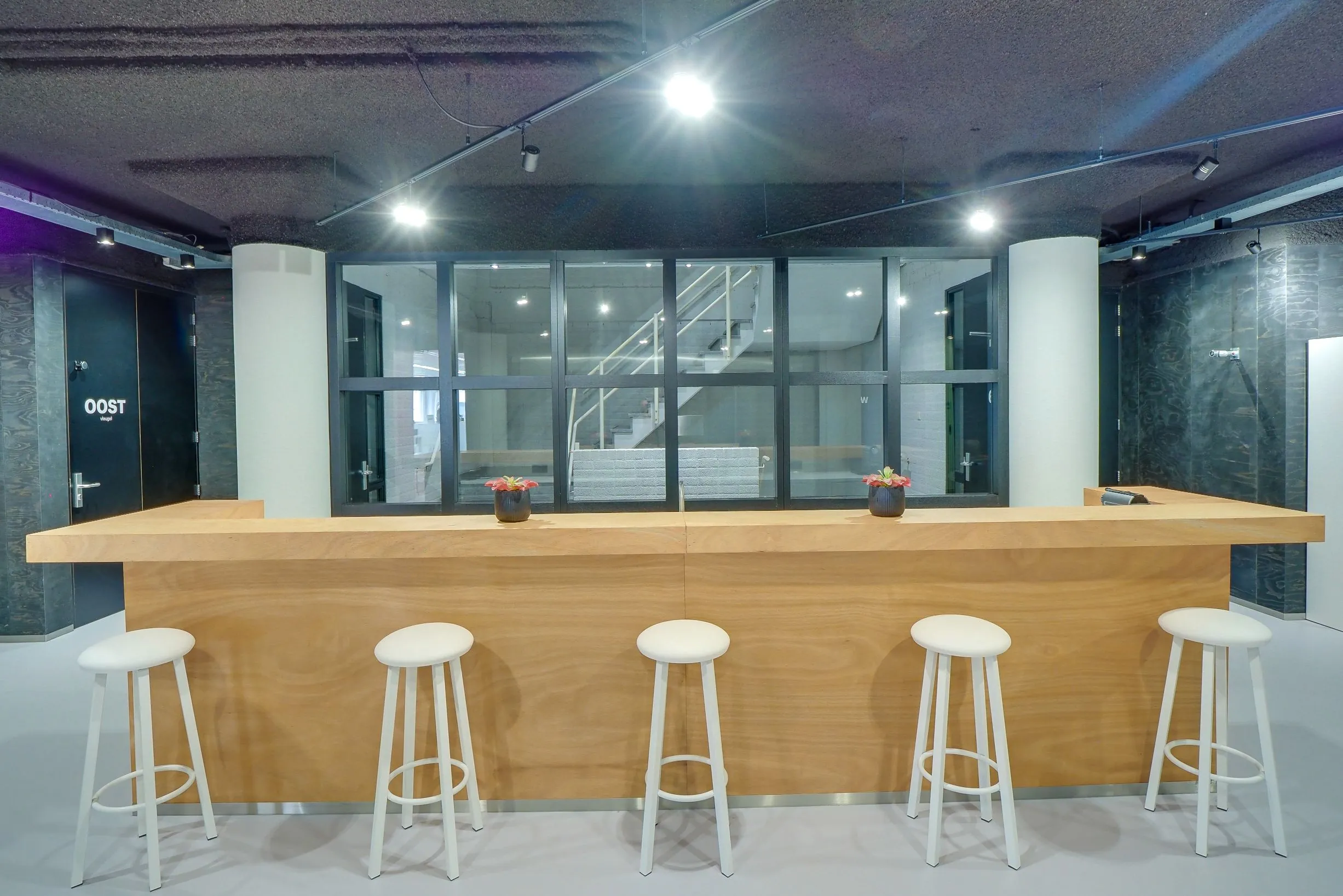 Houten balie met vijf witte barkrukken en twee bloempotjes in moderne interieurruimte van Europalaan 400.