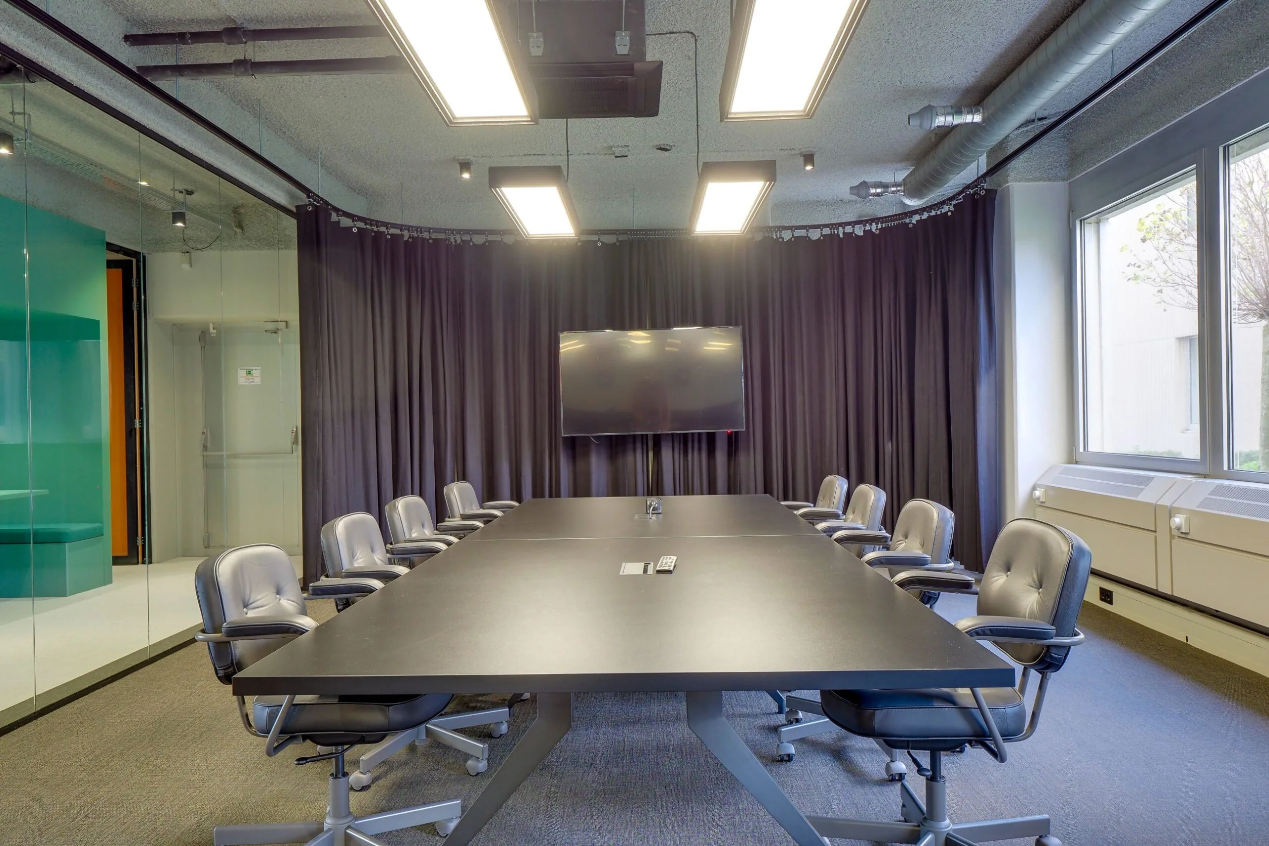 Moderne vergaderruimte aan de Europalaan 400 met een lange tafel, twaalf stoelen, een groot scherm en zwart gordijn.