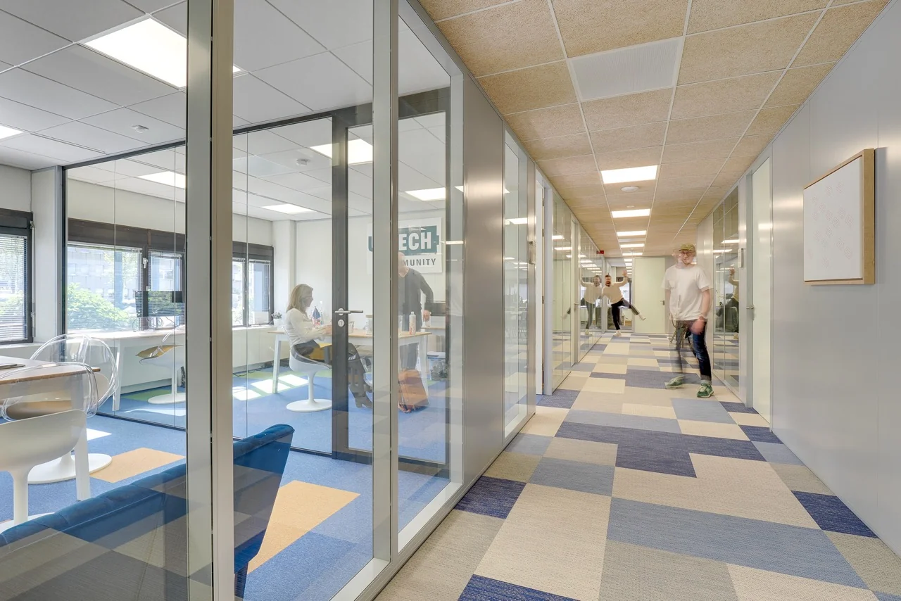 Moderne kantoorruimte aan de Europalaan 93 met glazen vergaderruimtes en blauwe vloerbedekking in een lichte gang.