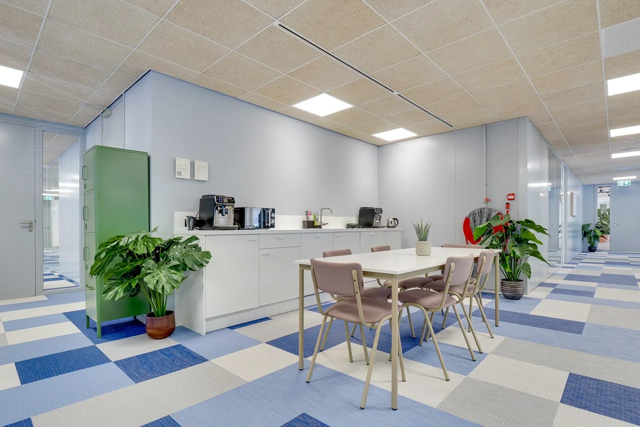 Moderne kantoorpantry met koffiemachine, zitgedeelte en kleurrijke vloer op Europalaan 93.
