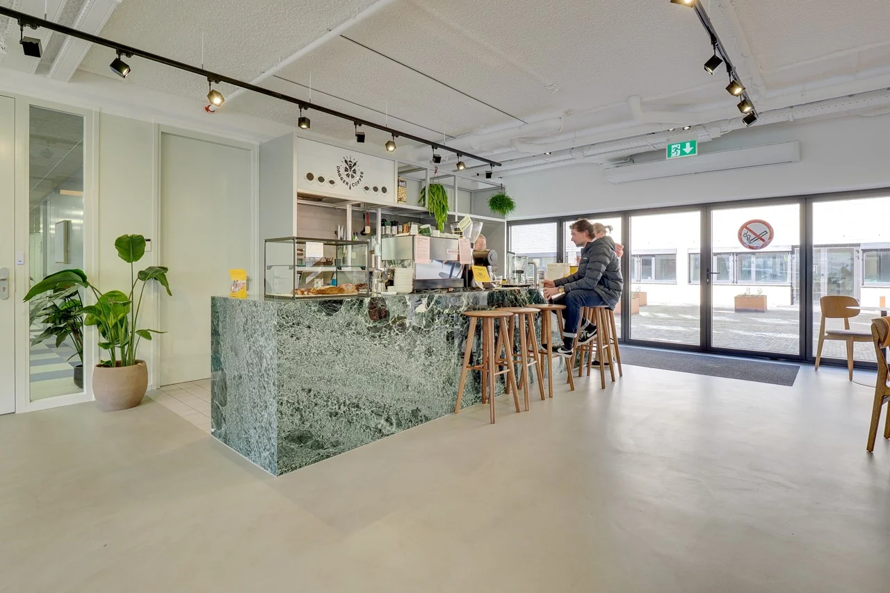 Moderne koffiezaak met marmeren balie, houten barkrukken en grote ramen aan de Europalaan 93.