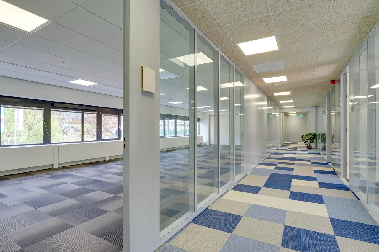 Moderne kantoorruimte aan de Europalaan 93 met glazen wanden en blauwgrijs tapijt in geometrisch patroon.