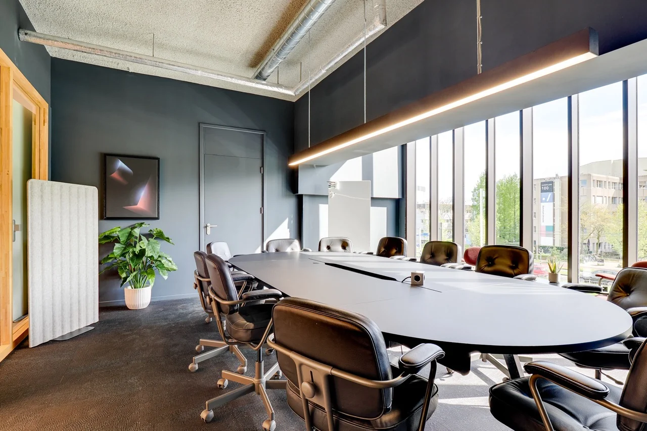 Vergaderruimte met ovale tafel, zwarte bureaustoelen en grote ramen in kantoor aan de Europalaan 93.