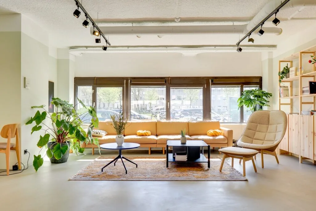 Lichte en moderne zithoek met een lange gele bank, planten en grote ramen in Europalaan 93.