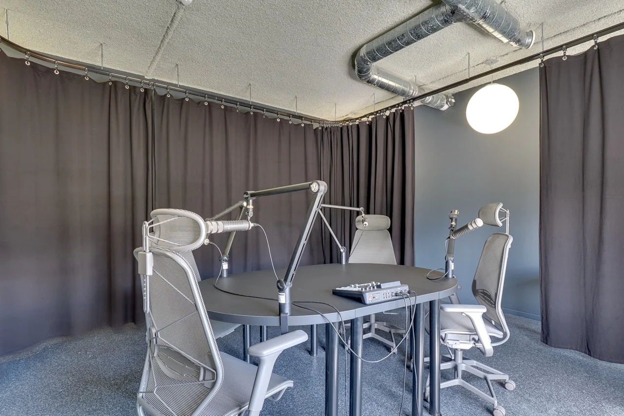 Moderne podcaststudio aan de Europalaan 93 met ronde tafel, microfoons, bureaustoelen en geluidsdempende gordijnen.