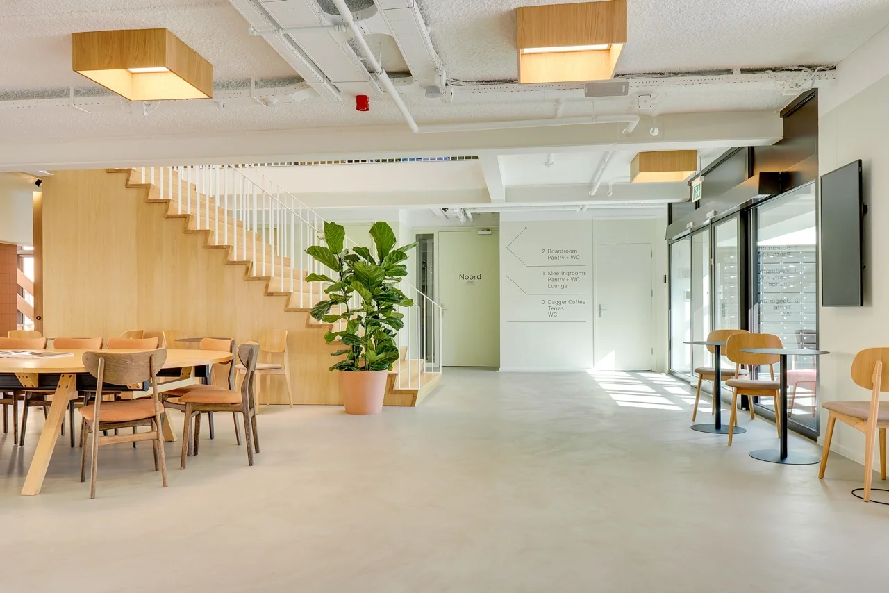 Moderne en lichte kantoorruimte aan de Europalaan 93 met houten trap, ronde vergadertafel, planten en zitplekken langs de glazen wand.