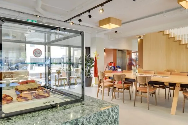 Moderne, lichte horecaruimte aan de Europalaan 93 met houten meubilair, een gebaksvitrine en een open zitgedeelte.