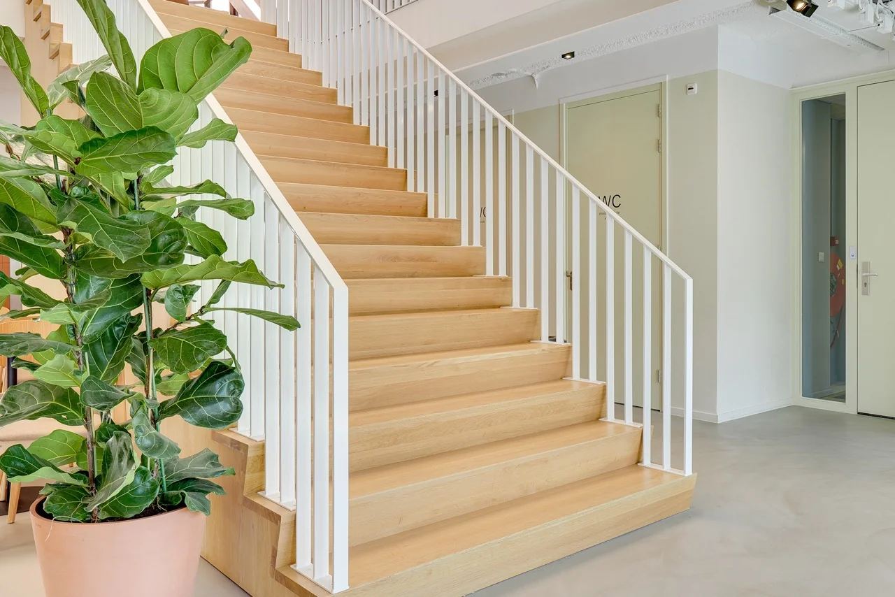 Houten trap met witte leuningen in een modern interieur aan de Europalaan 93, met een grote groene kamerplant op de voorgrond.