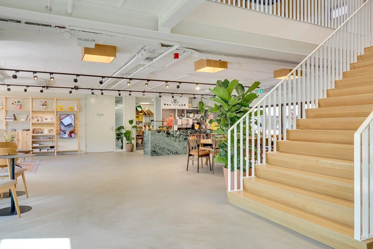 Moderne en lichte kantoorlobby met houten trap, groene planten, koffiebar en zitgedeelte aan de Europalaan 93.