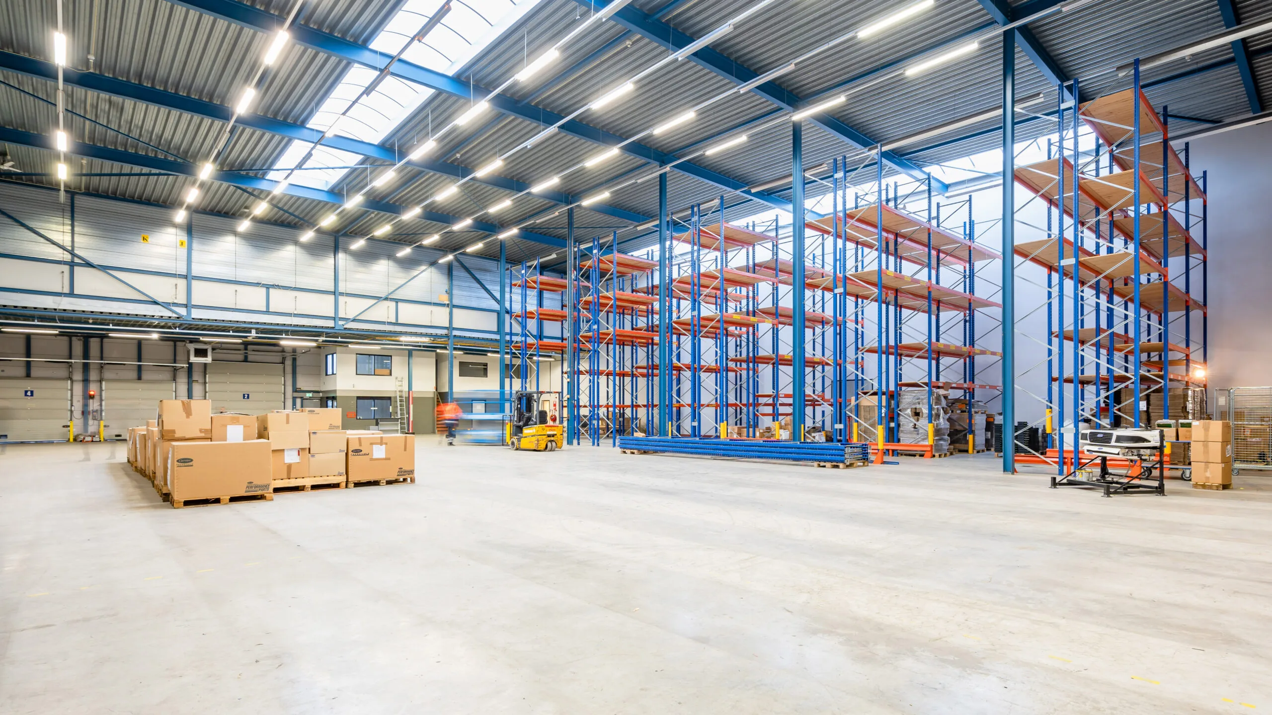 Ruime en goed verlichte magazijnhal met lege stellingen en stapels kartonnen dozen op pallets.
