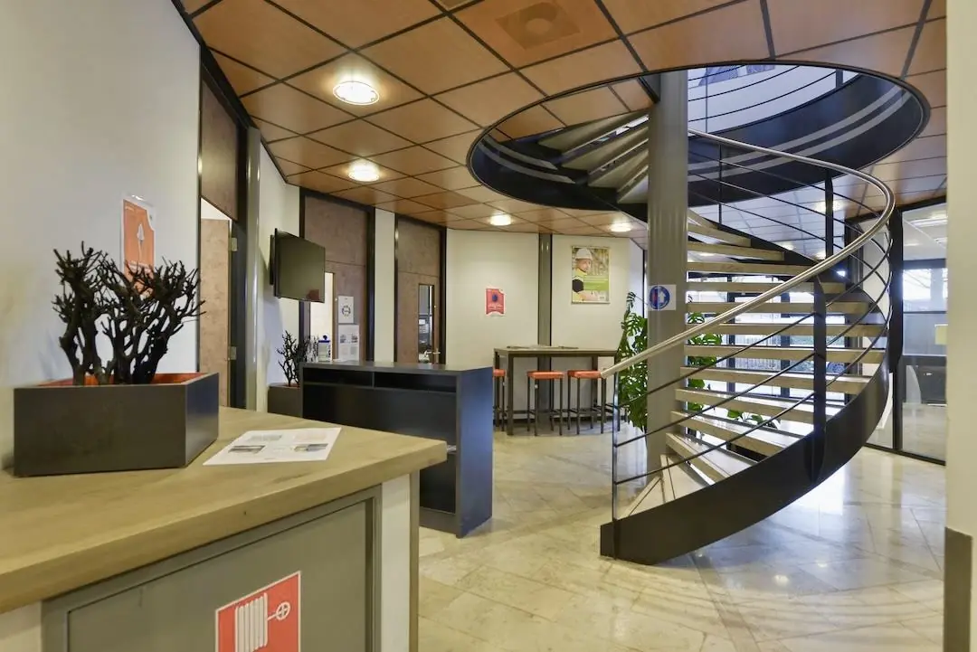 Moderne kantoorruimte in FlexOffiZ Amersfoort met een opvallende wenteltrap en een zitgedeelte met hoge tafels en barkrukken.