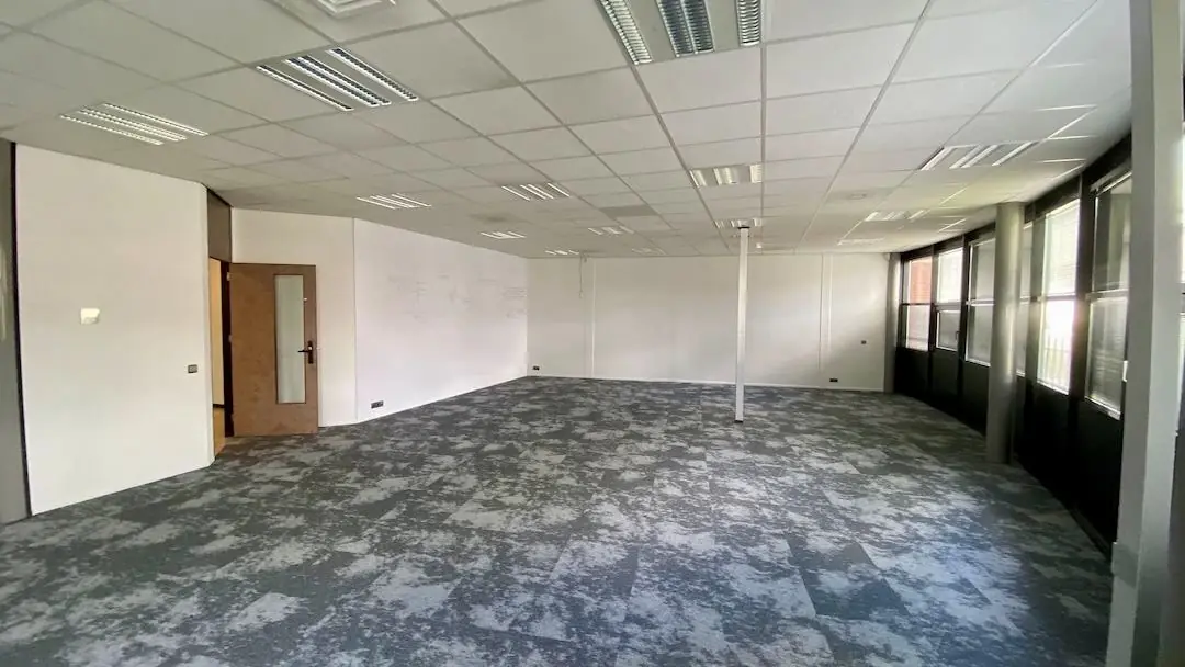 Lichte, lege kantoorruimte met grote ramen en grijs patroonvloer in FlexOffiZ Amersfoort aan de Heliumweg 22.