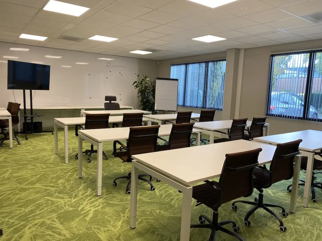 Moderne vergaderruimte bij FlexOffiZ Amersfoort aan de Vanadiumweg met bureaus, stoelen, een whiteboard en een scherm.