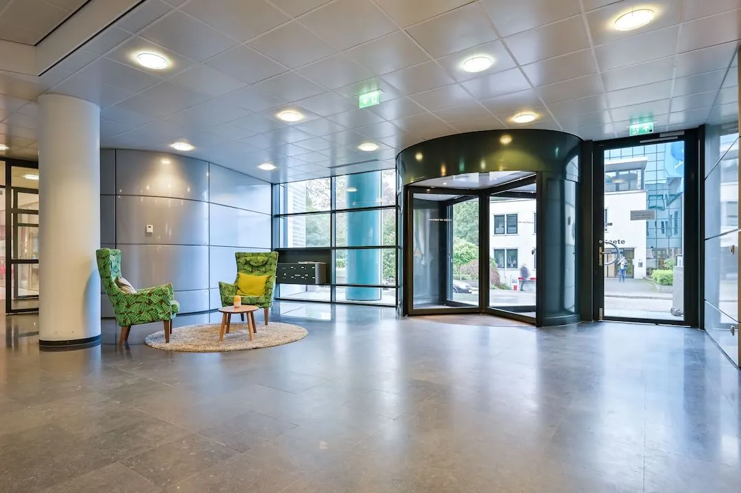 Moderne entreehal van FlexOffiZ Baarn met glazen draaideur, zitgedeelte en veel natuurlijk licht.