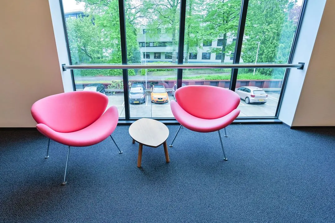 Twee roze designstoelen met een klein houten tafeltje ertussen bij het raam in FlexOffiZ Baarn.