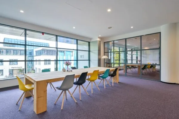 Moderne vergaderruimte bij FlexOffiZ Baarn met lange houten tafel, kleurrijke stoelen en grote ramen met uitzicht op Parkstaete.