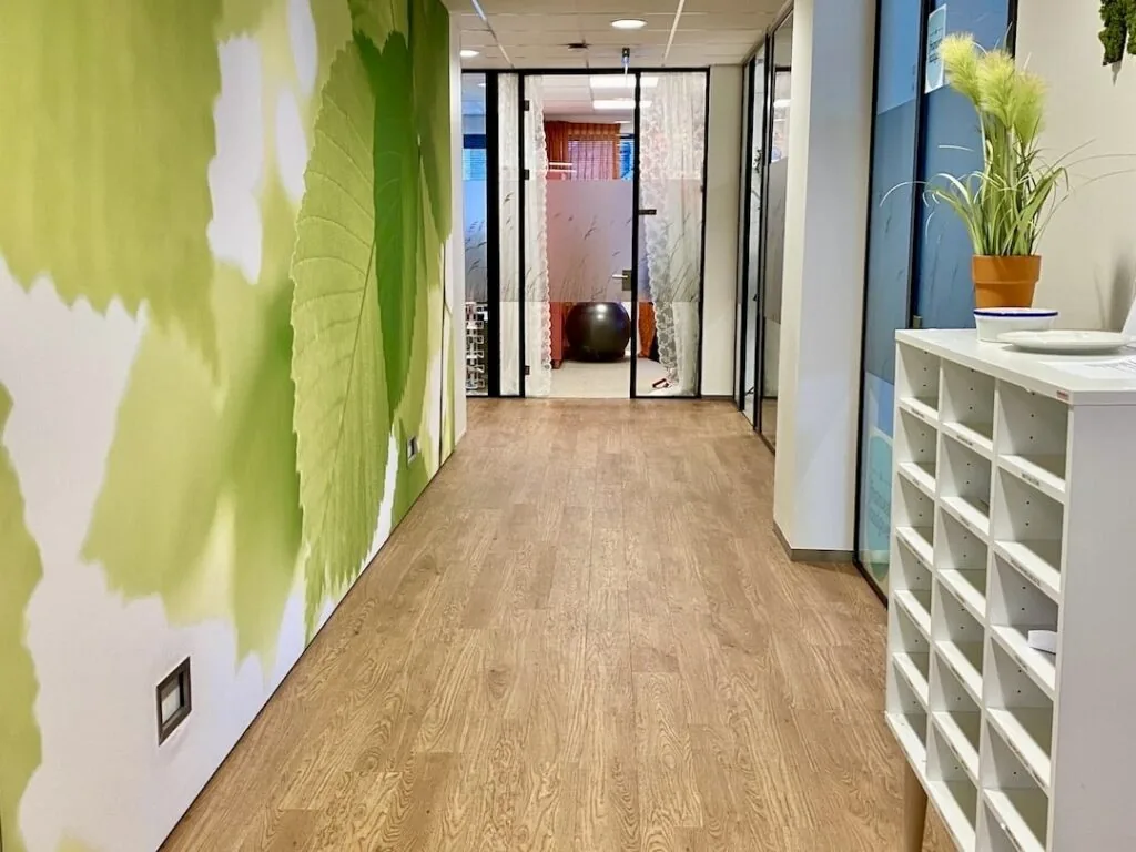 Moderne gang in FlexOffiZ Bodegraven met houten vloer, wanddecoratie met groene bladeren en glazen kantoorwanden.