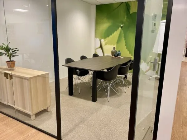 Vergaderruimte bij FlexOffiZ Bodegraven met een houten tafel, zwarte stoelen en een wanddecoratie van een groene bladprint.