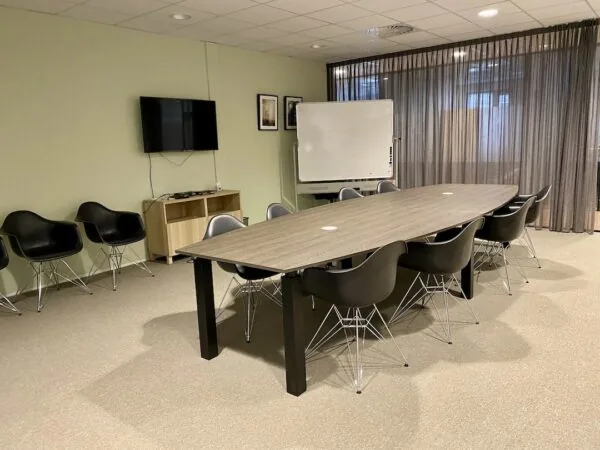Vergaderruimte bij FlexOffiZ Bodegraven met een lange tafel, zwarte stoelen, een whiteboard en een tv aan de muur.