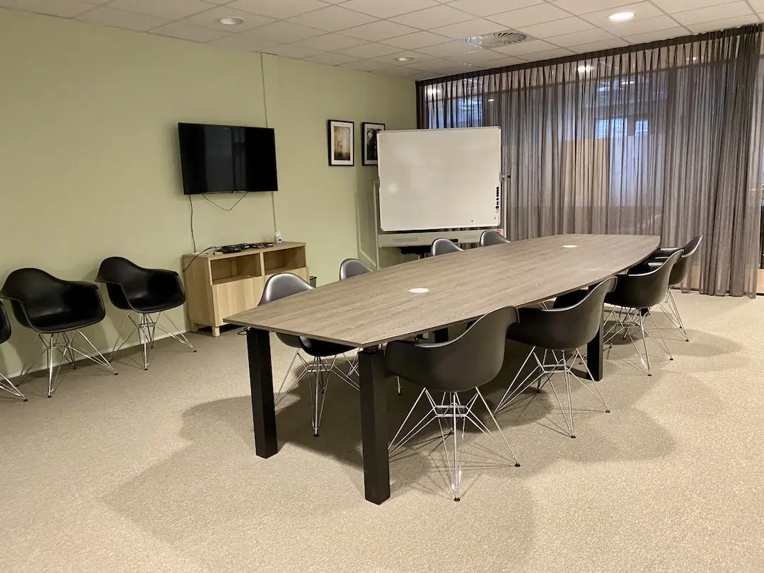 Vergaderruimte bij FlexOffiZ Bodegraven met een lange tafel, zwarte stoelen, een whiteboard en een tv aan de muur.